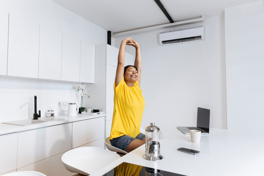 Happy woman stretching in kitchen taking a break fron freelance work