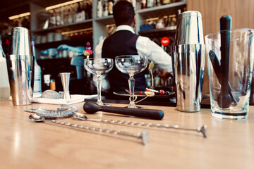 Bar equipment and glasses arranged on counter with bartender in background