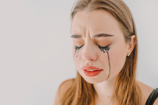 Sad young woman with smudged mascara crying in front of wall