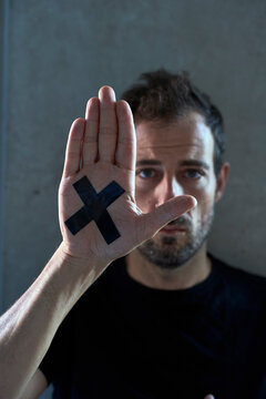 Man showing hand with cross marking in front of wall