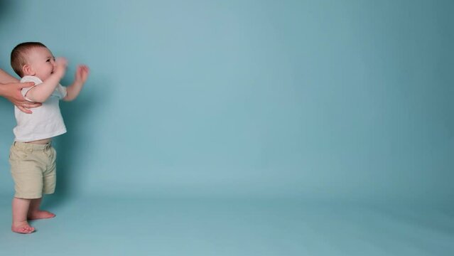 Happy toddler baby learns to walk and takes his first steps. Child boy walks for the first time on a studio blue background. Kid age one year, slow motion