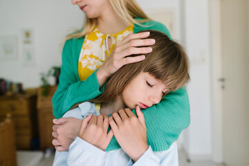 Mother hugging sad daughter from behind at home