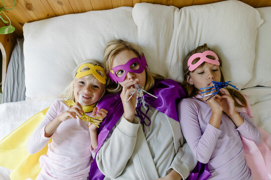 Mother and daughters with party horn blower lying on bed at home