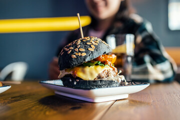 Black bun burger served at table with woman in background