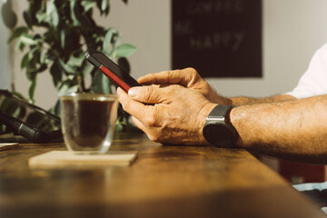 Hands of businessman wearing smart watch using mobile phone at office coffee corner