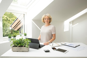 Confident businesswoman standing at desk in home office