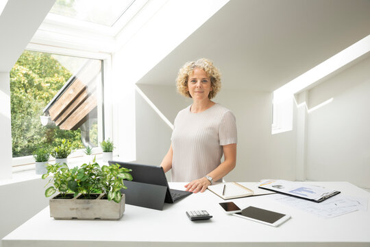 Confident businesswoman standing at desk in home office
