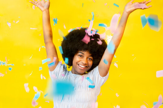 Happy young woman throwing confetti against yellow background