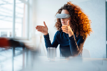 Businesswoman wearing virtual reality simulator sitting with semiconductor at desk in office