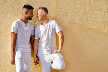 Cheerful gay couple holding hands in front of wall on sunny day