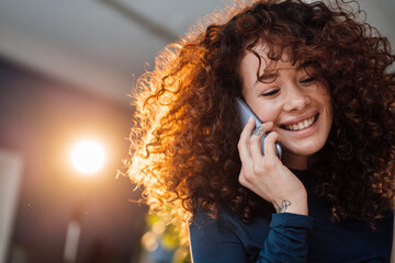 Happy beautiful woman with curly hair talking on mobile phone