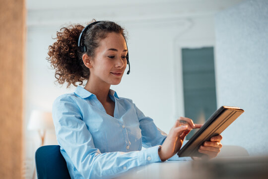 Smiling customer service representative using tablet PC sitting at desk in office
