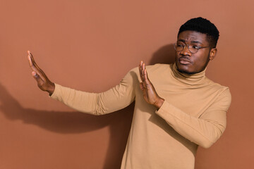 Portrait of handsome trendy skeptic guy showing aside stop sign isolated over brown color background