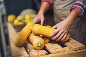 Woman works in fruits and vegetables shop. She is stacking goods in storefront.