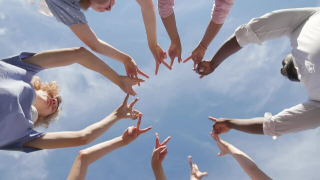 Bottom view of multiethnic teen students making finger circle outdoors