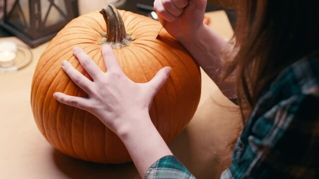 Preparing pumpkin for Halloween. Woman sitting and carving with knife halloween Jack O Lantern pumpkin at home for her family.