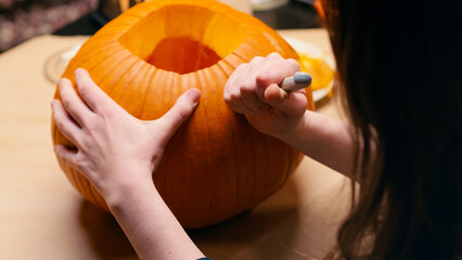 Preparing pumpkin for Halloween. Woman sitting and carving with knife face details of halloween Jack O Lantern pumpkin at home for her family.