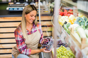 Woman works in fruits and vegetables shop. She is examining goods.