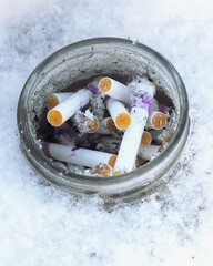 Cigarette butts are stacked in a dirty glass jar. The ashtray is placed in a snowdrift. Protection of nature and the environment from pollution. Vertical illustration. Harm from smoking