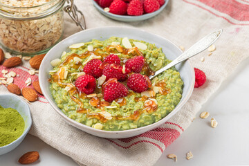 Oatmeal matcha porridge in bowl with fresh ripe raspberries, nuts and caramel sauce for healthy breakfast