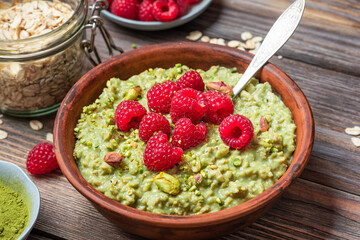 Healthy breakfast. Oatmeal matcha porridge with fresh raspberries and pistachios in a bowl on rustic wooden table