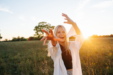 Overjoyed young blond woman standing amidst wheat field. Reaching with her hand