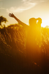 Smiling young blond woman standing amidst wheat field. Against setting sun