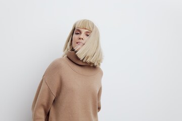 an attractive woman stands on a light background in a sweater and shirt, gently looking down with...