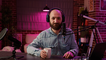 Fototapeta na wymiar Portrait of online radio host recording podcast for entertainment show using professional audio equipment and microphone in home studio. Man influencer posing casual talking in internet broadcast.