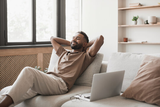 Satisfied Handsome Young Man Relaxing On The Sofa At Home In The Living Room, Resting After A Hard Day Work, Closed His Eyes, Put His Hands Behind His Head, Smiles Happily