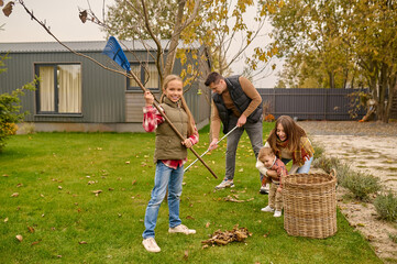 Whole family cleaning their yard in autumn