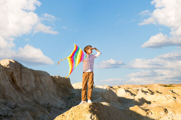 Portrait of child 8-9 years old with a kite. A blond boy stands and looks into the distance from a high mountain.