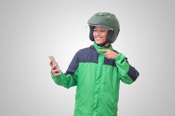 Portrait of Asian online taxi driver wearing green jacket and helmet holding mobile phone and pointing to empty space with finger. Isolated image on white background