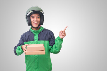 Portrait of Asian online courier driver wearing green jacket and helmet delivering package and box while pointing away with finger. Isolated image on white background