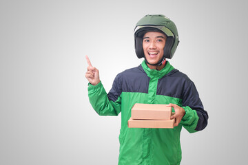 Portrait of Asian online courier driver wearing green jacket and helmet delivering package and box while pointing away with finger. Isolated image on white background