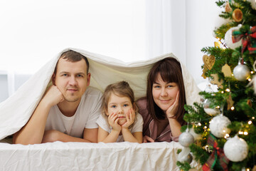 christmas, family and love concept - happy family lying under blanket