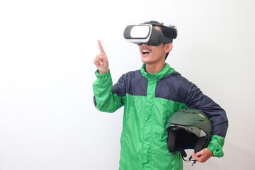 Portrait of Asian online taxi driver wearing green jacket and holding a helmet while using virtual reality or VR and pointing. Isolated image on white background