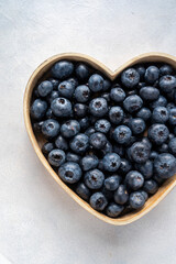 Blueberries berry in heart shaped bowl, on bright background. Healthy food template, mockup with copy space.