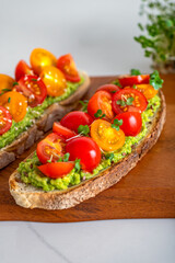 Fototapeta na wymiar Tasty open sandwich from toasted sourdough bread with mashed avocado and fresh tomatoes