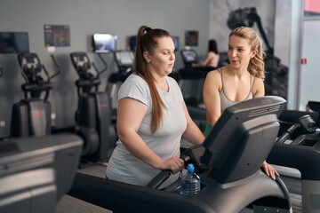 Caucasian instructor helping plus size woman at the gym