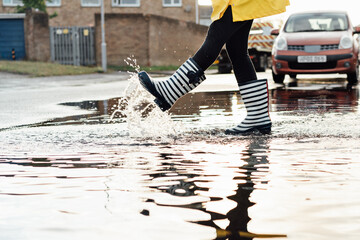 Woman having fun on the street after the rain. Close up female legs in rain rubber boots walking...