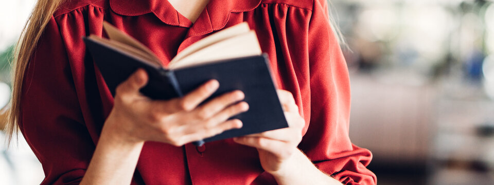 Close-up of woman reading book in red and black smart-casual dress