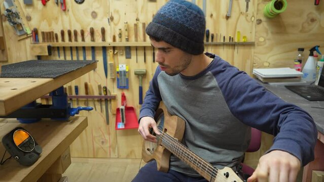 Luthier in workshop tunes newly built custom electric resonator guitar with digital tuner