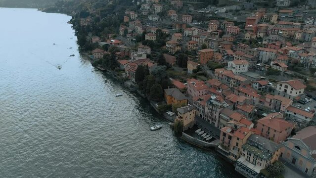 Aerial tilt over lake como village side showing mediterranean houses architecture with alp mountains in the background - moody cinematic
