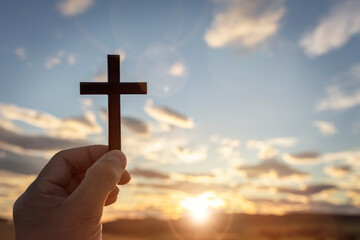 Holding up religious cross crucifix to sky at sunset background