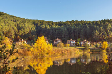 Fototapeta na wymiar Autumn landscape with traditional bulgarian houses, lake and reflection of colorful trees, Bulgaria Rhodope mountains