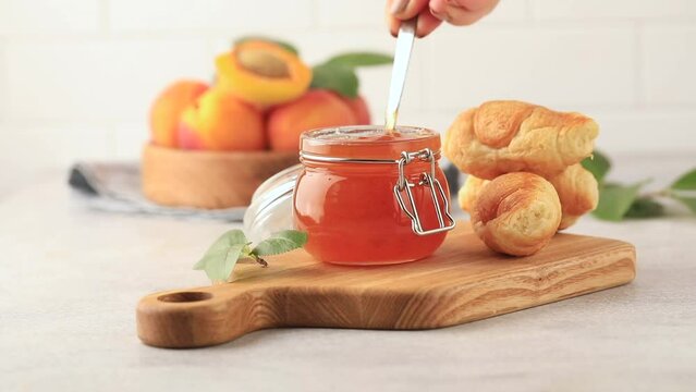  Apricot jam in a jar is stirred with a spoon. Fruit preservation.