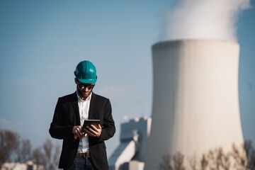 Electric engineer wearing helmet suit and safety vest coal fired power station in background at...