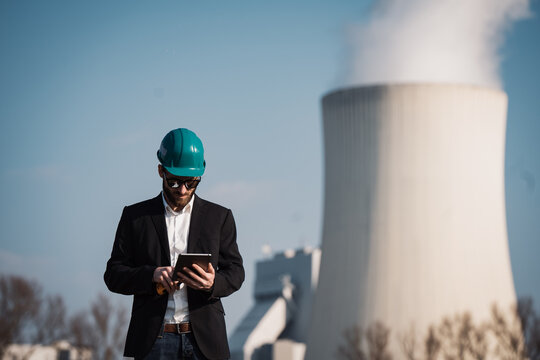 Electric engineer wearing helmet suit and safety vest coal fired power station in background at energy crisis