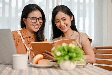 Two Asian female college students reading a book together in the coffee shop.